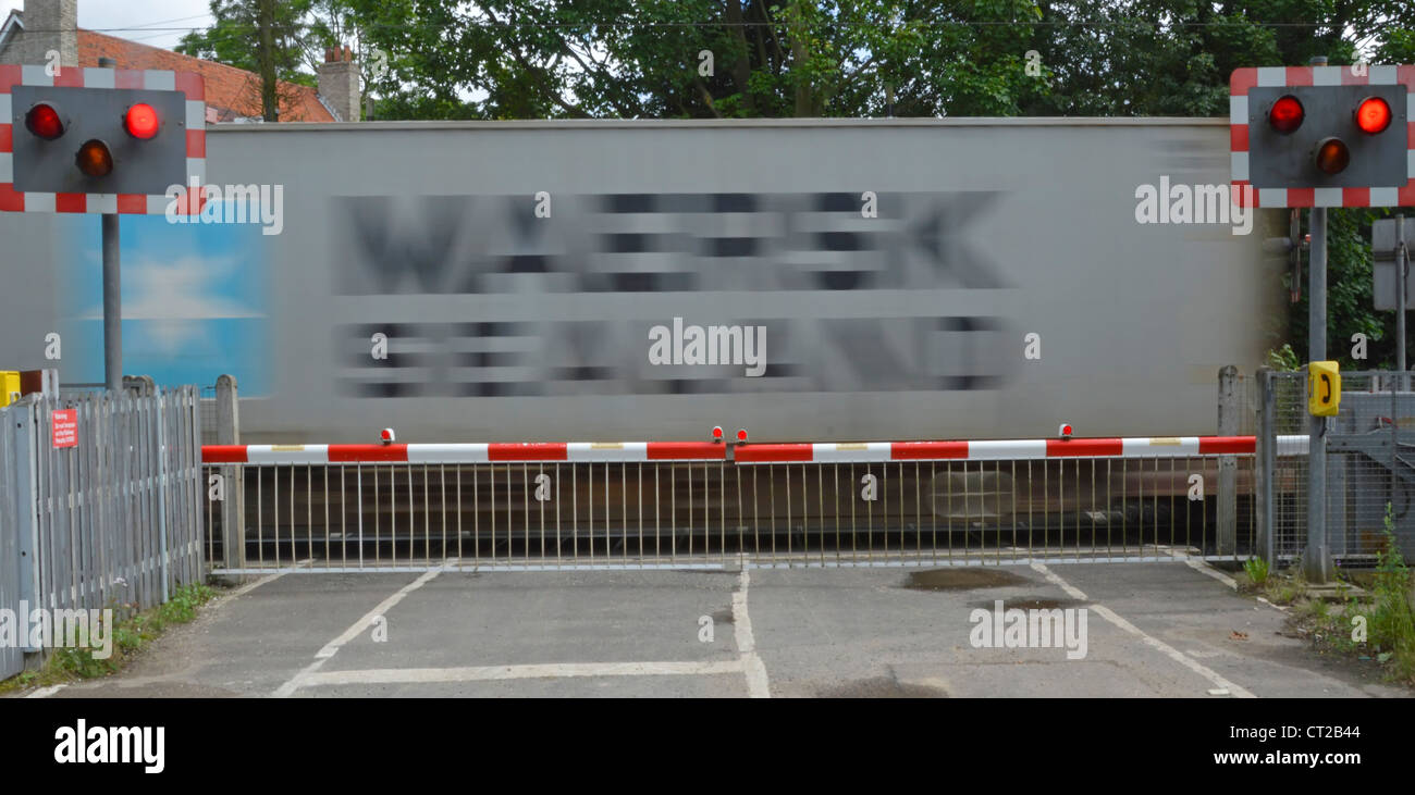 Railway tracks red flashing warning light sign level crossing barrier gates country road container train motion blur Margaretting Essex England UK Stock Photo