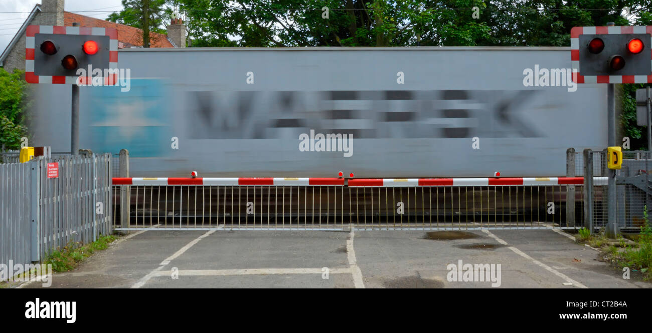 Railway tracks red flashing warning light sign level crossing barrier gates country road container train motion blur Margaretting Essex England UK Stock Photo