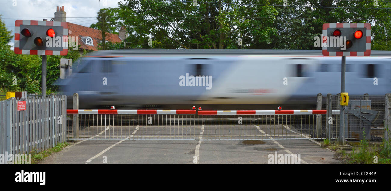 Railway tracks red flashing warning light sign level crossing barrier gates country road passenger train motion blur at Margaretting Essex England UK Stock Photo