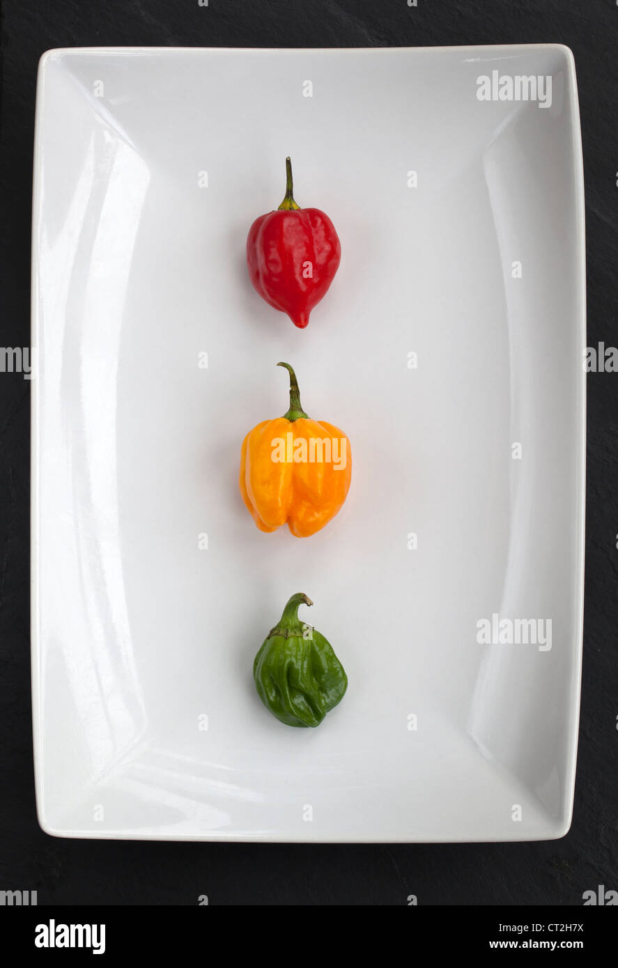 Three Multi Coloured Scotch Bonnet Chilli Peppers on white plate Stock Photo