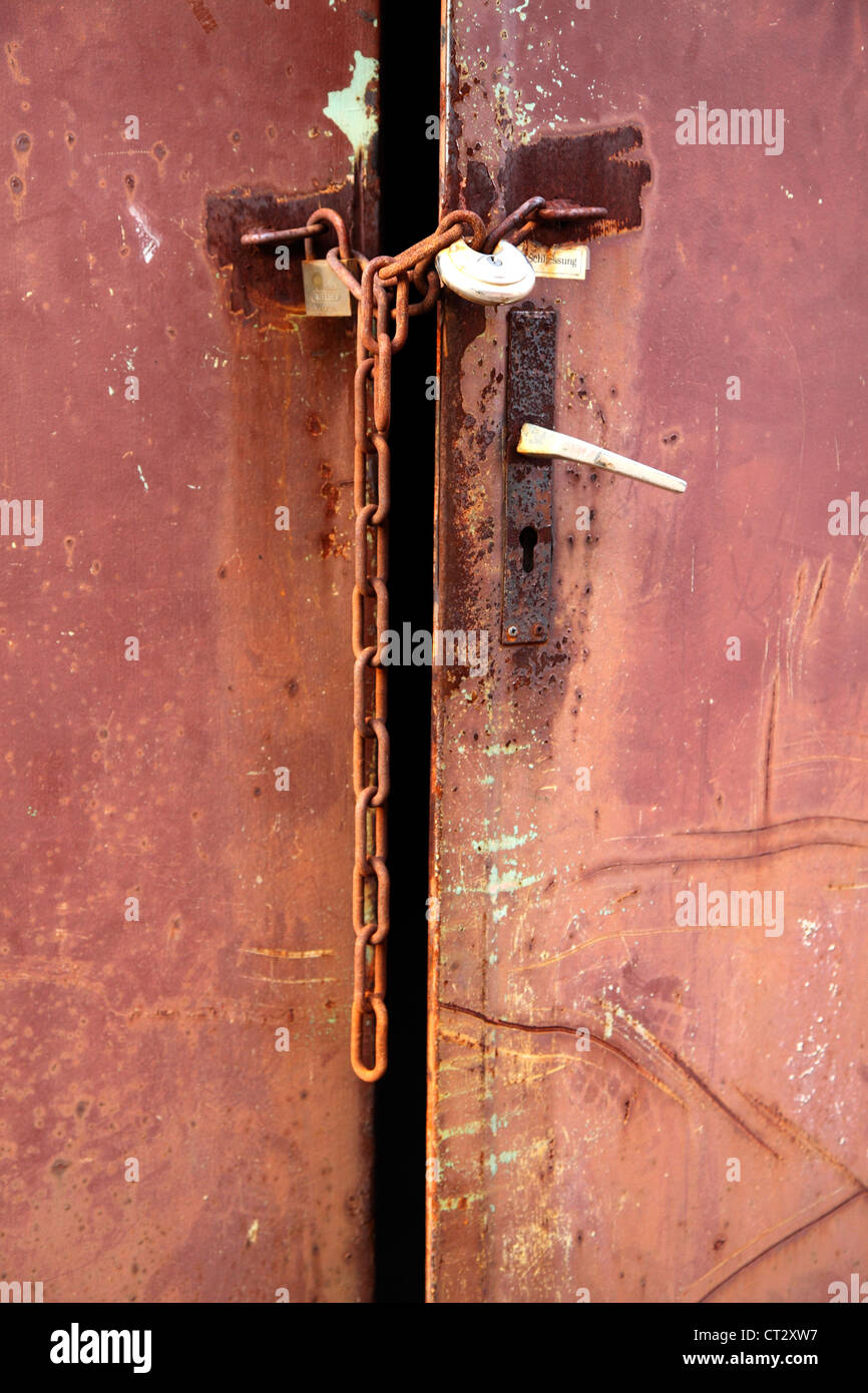 Red, rusty metal door, locked with an iron chain. Stock Photo