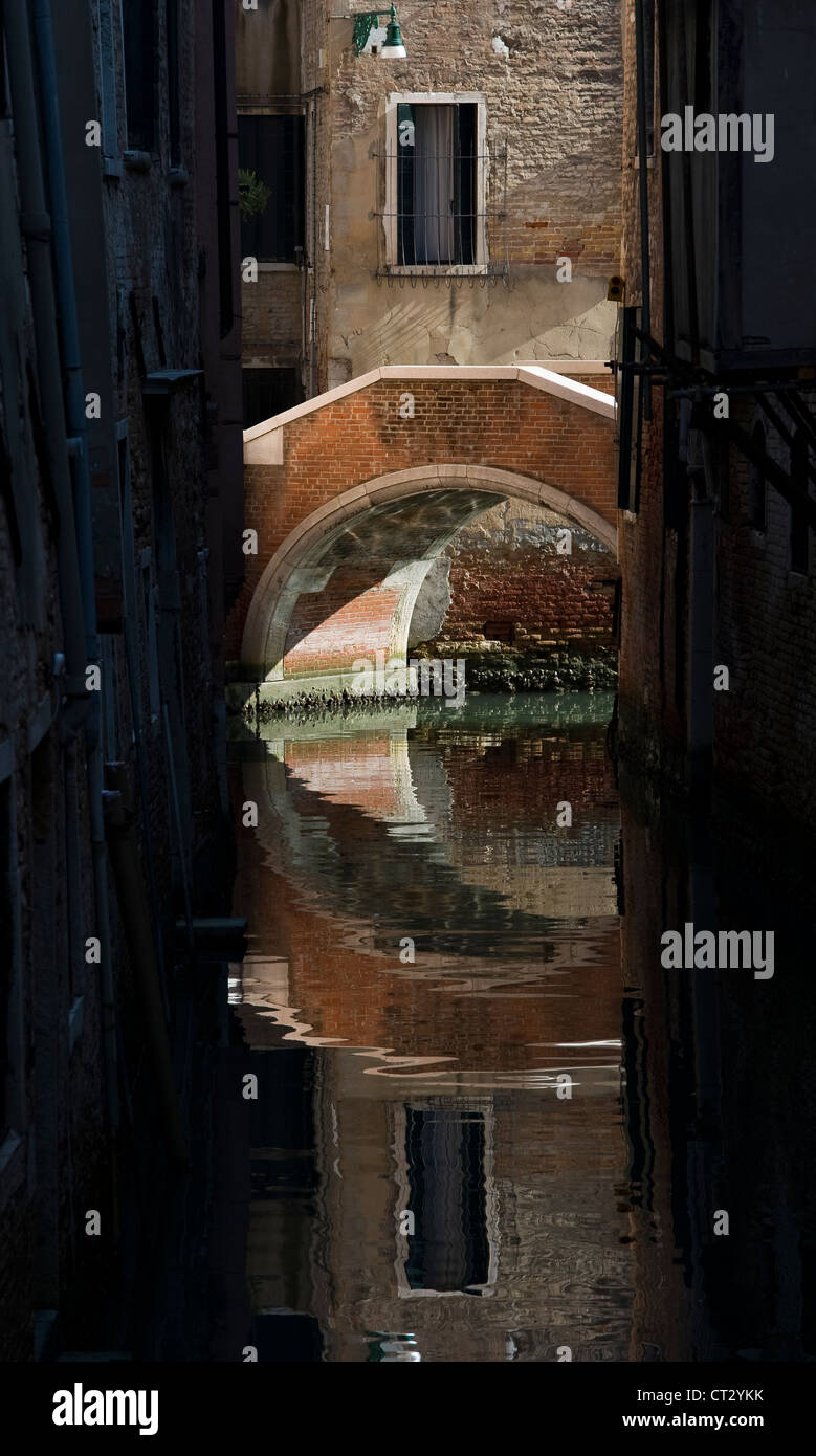 A footbridge reflected in a quiet canal in the back streets of Venice, Italy Stock Photo