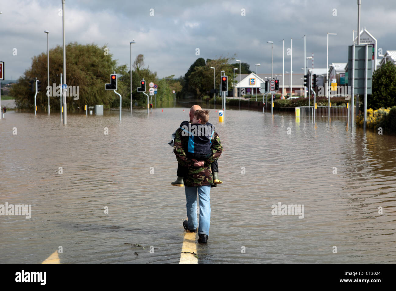 A man carries his son and walks through the flooded roads of Weymouth after torrential rain in Dorset Stock Photo
