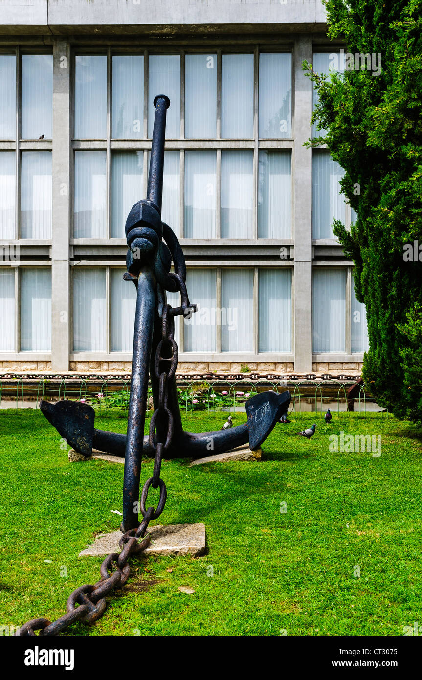 A large black iron ship's anchor attractively situated on the lawn in front of one of the halls of the Maritime Museum, Lisbon Stock Photo