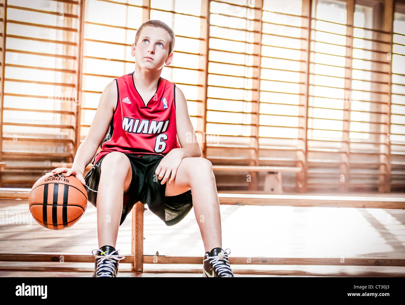 Teenager boy sitting on wooden bench holding basketball in basketball ...
