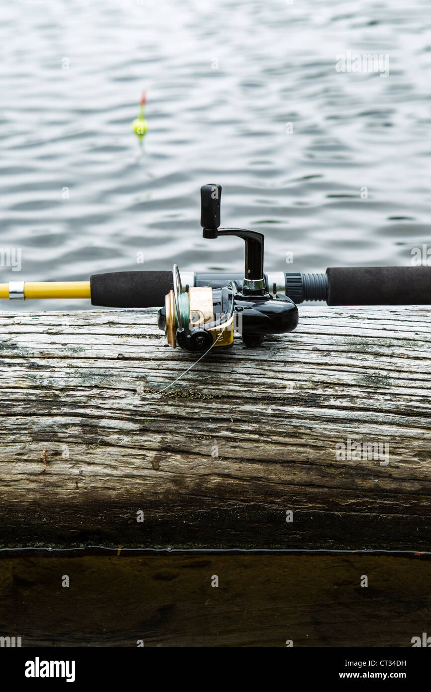 Fishing reel, rod on log with water and bobber in background Stock Photo