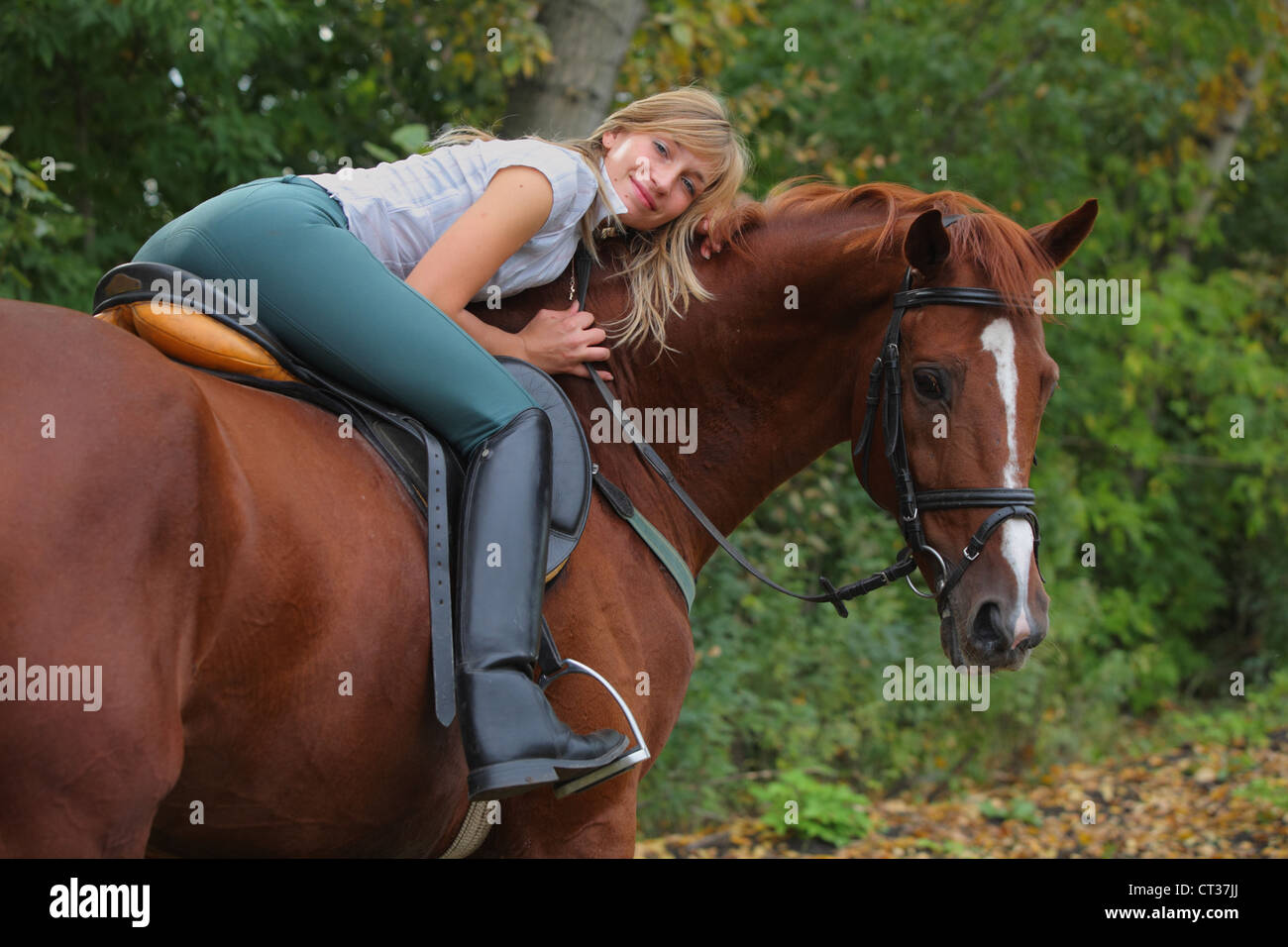 Young women in riding dresses posing with bay horse in a wooded area