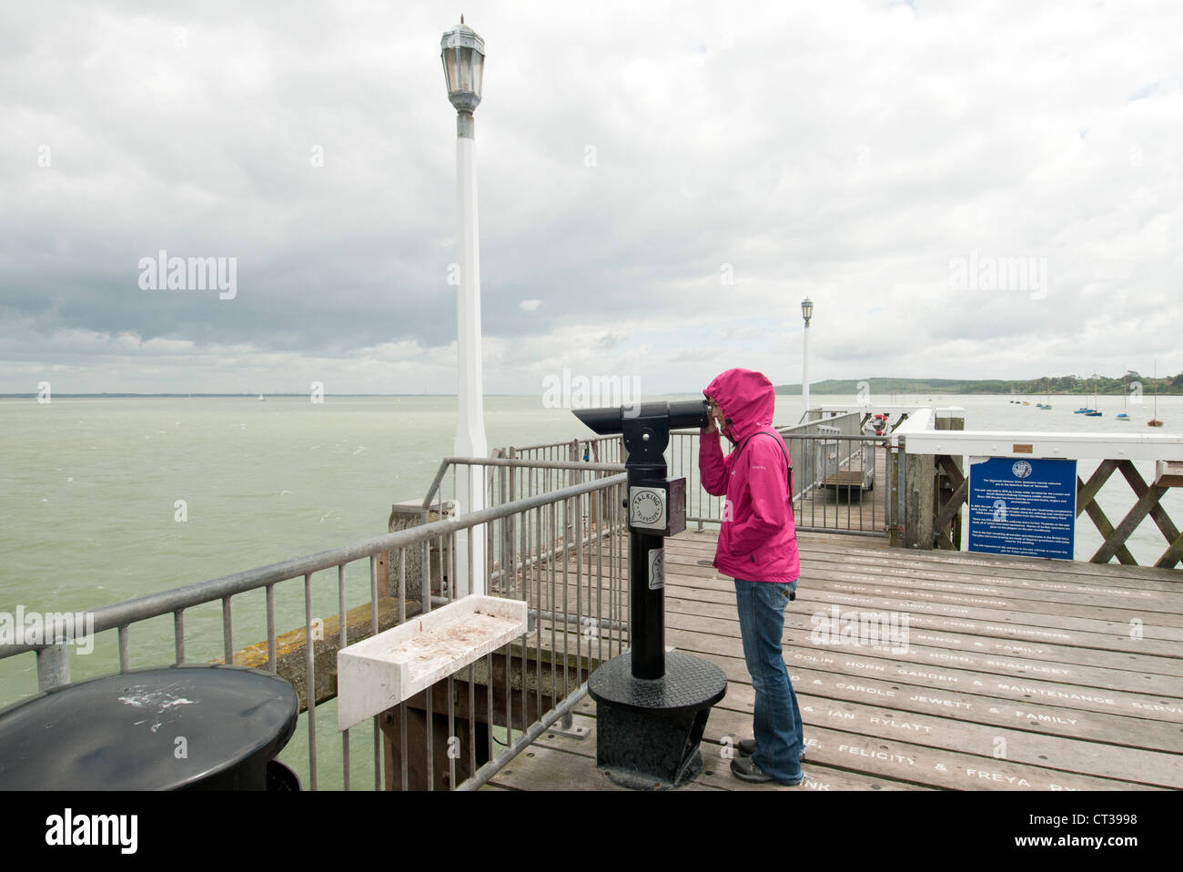 woman looking through a telescope at the end of Yarmouth Pier on the Isle of Wight Stock Photo