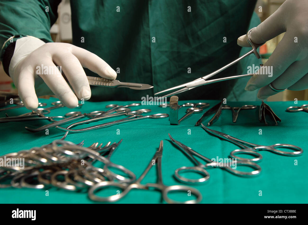 Close-up on the hands of a surgeon holding a scalpel and a pair of forceps over a table laden with various surgical tools. Stock Photo