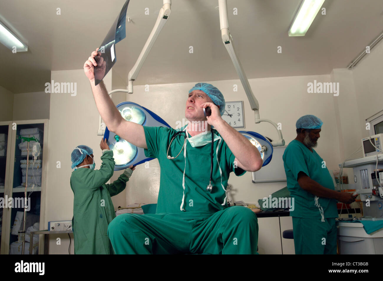 A busy surgeon examines an x-ray while talking on his phone Stock Photo