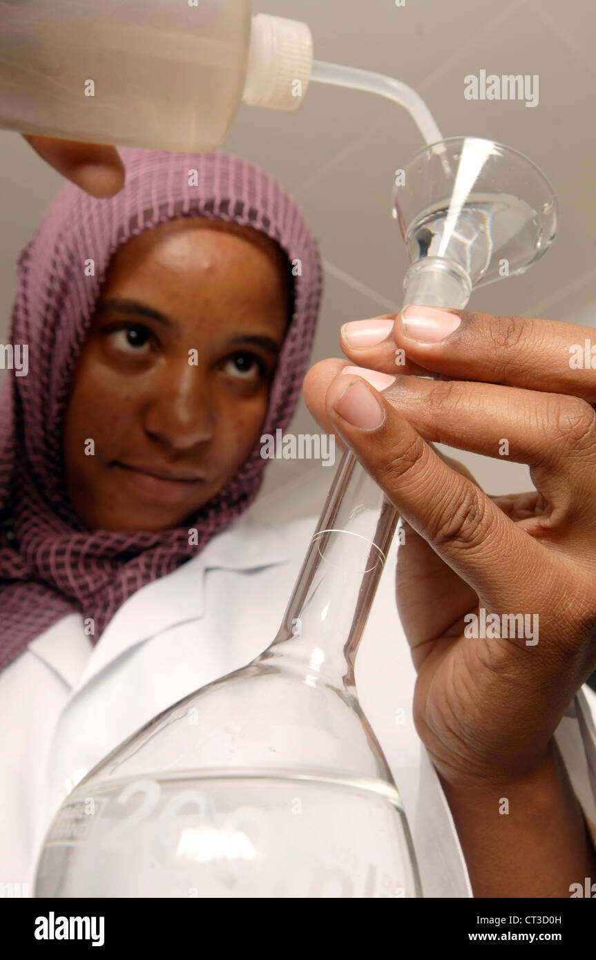 A female laboratory technician in a pharmaceutical factory pouring a chemical solution into a volumetric flask. Stock Photo