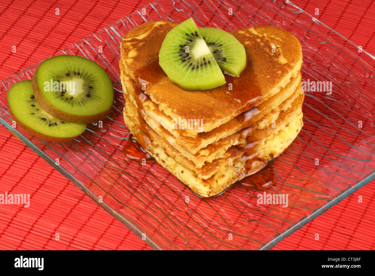 Heart-shaped pancakes with syrup and kiwi fruit on a transparent glass dish for Valentine's Day breakfast. Stock Photo