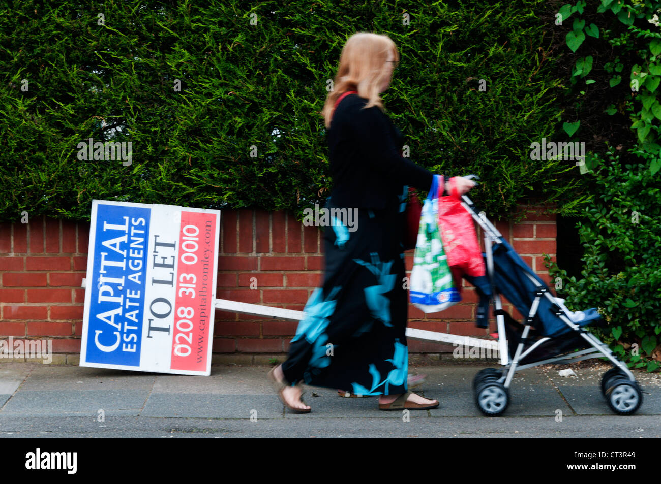 Estate Agents' sign passed by (motion blurred) woman with pushchair. Stock Photo