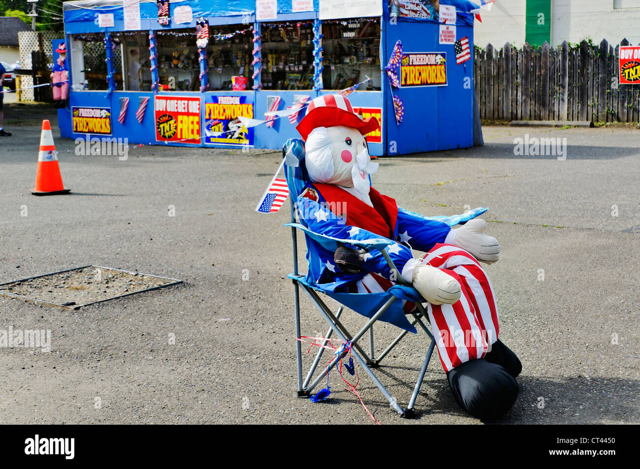 An inflatable life-size Uncle Sam figure sits in a chair in front of a fireworks stand with patriotic charm and appeal. Stock Photo