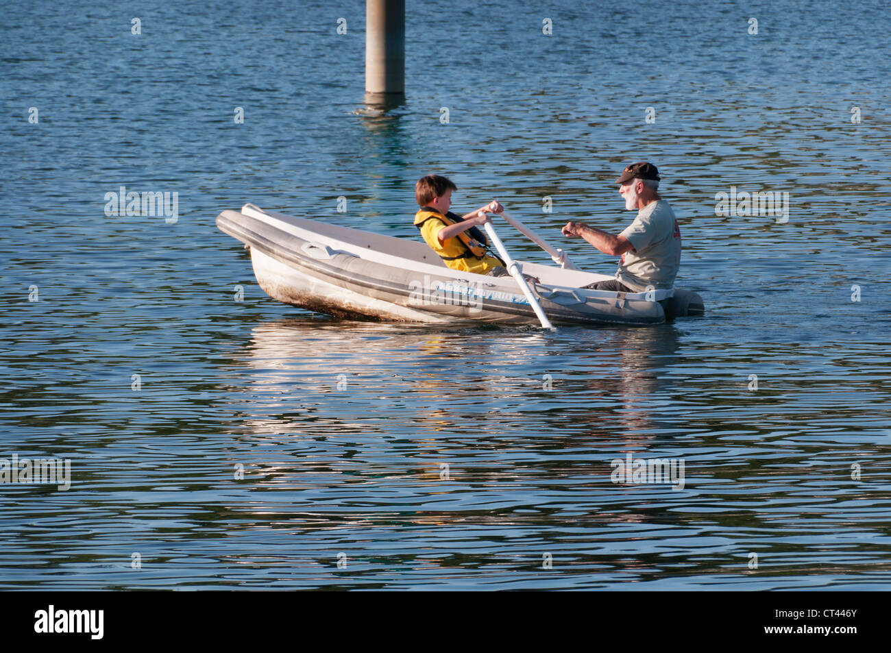 A little boy practices rowing with concentration and determination as he listens to his grandfather in a dinghy. Stock Photo