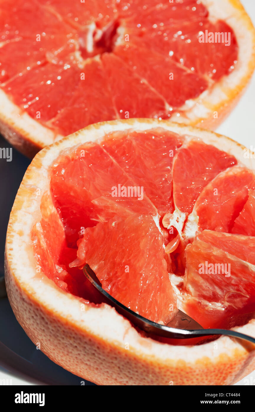 A spoon with a section of grapefruit rests on a cut grapefruit half with the other half in the background. Stock Photo
