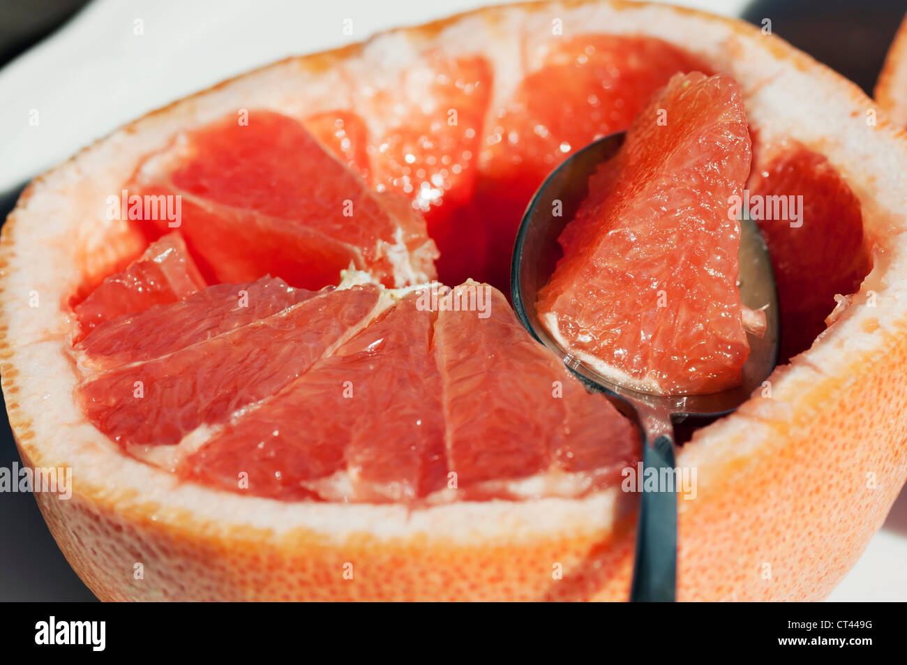 A spoon with a section of grapefruit rests on a cut grapefruit half. Stock Photo