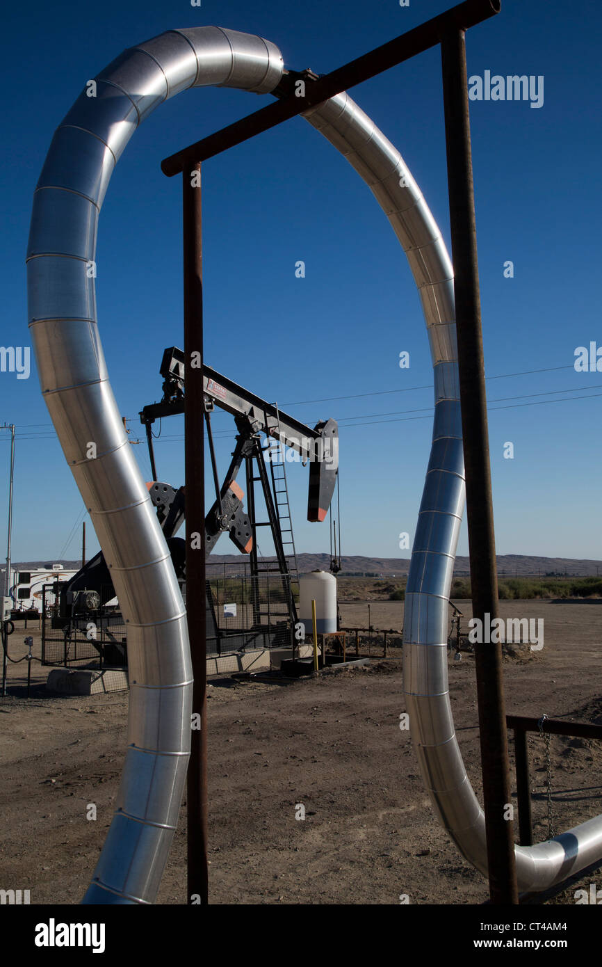 An expansion loop in a natural gas pipeline frames an oil well Stock Photo