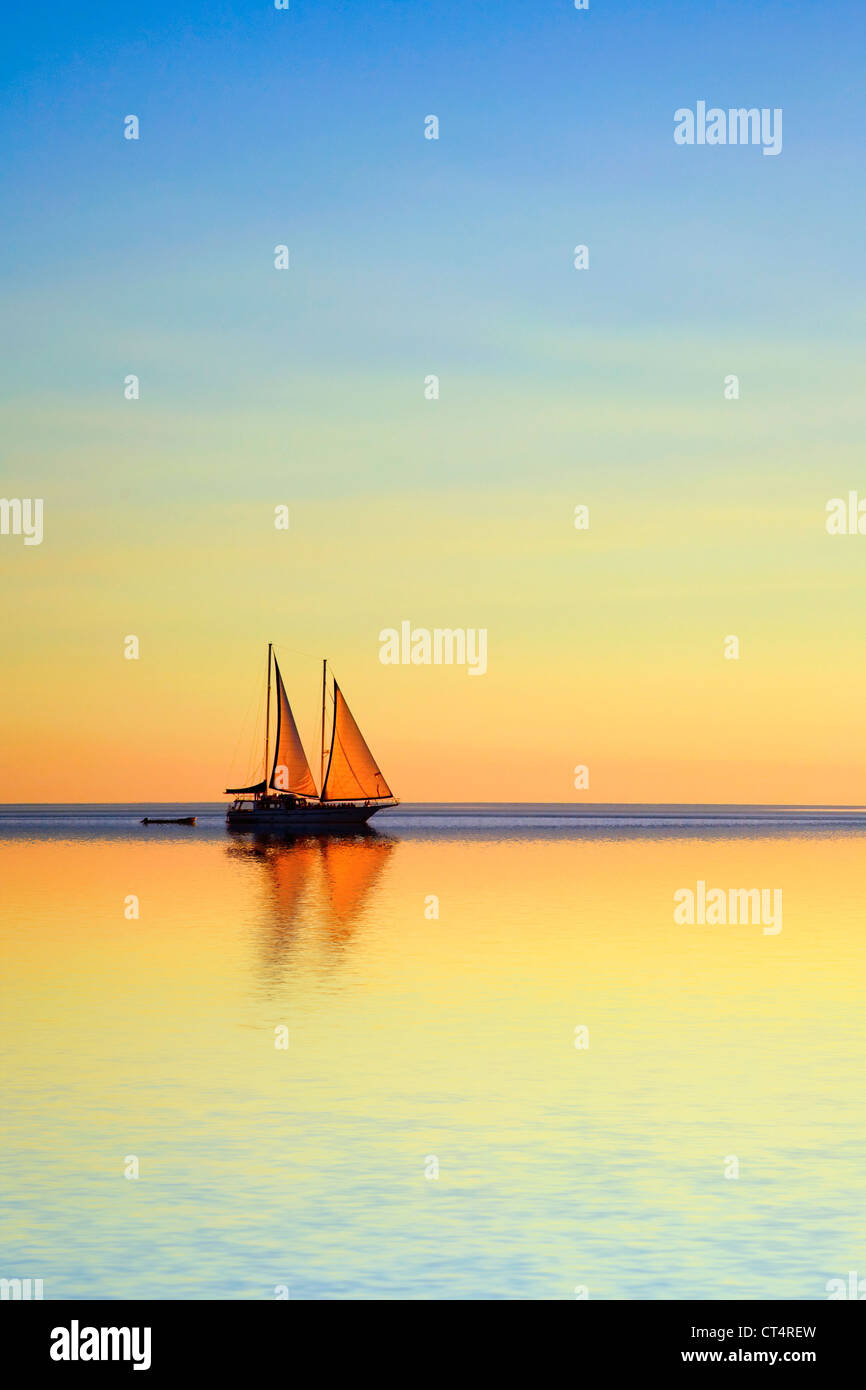 Romantic sailing boat reflected in tropical ocean at twilight. Stock Photo