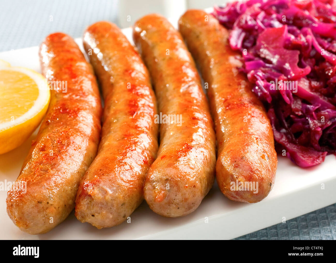 A platter with German Thuringer sausage or bratwurst, with spiced red cabbage and lemon. Stock Photo