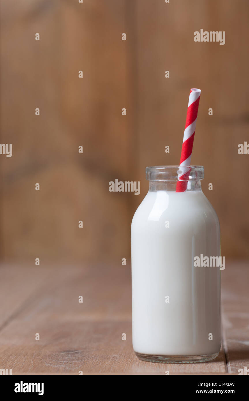 Single bottle of milk with red striped drinking straw in rustic setting Stock Photo