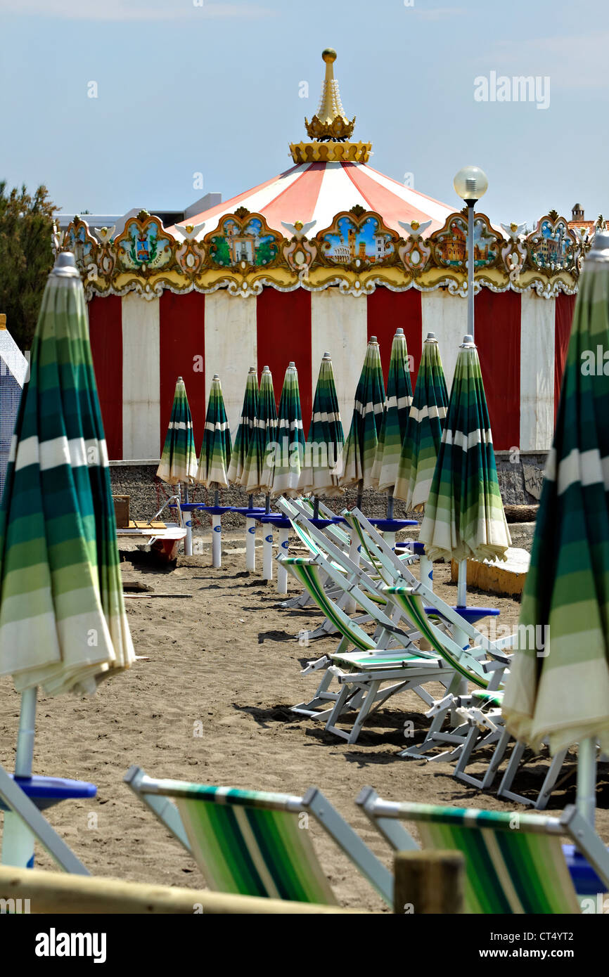 Carousel closed sun umbrellas ( beach umbrellas ) and chairs on a sandy beach, Cecina Mare, Tuscany Italy Stock Photo