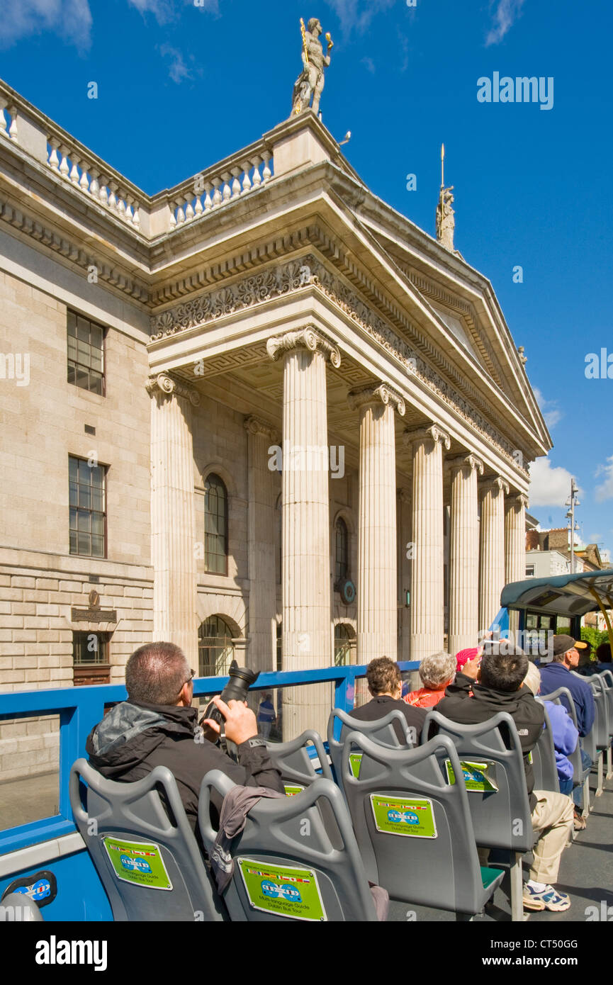 Tourists on top of a 'hop on hop off' city tour bus drive past the General Post Office on O'Connell Street. Stock Photo