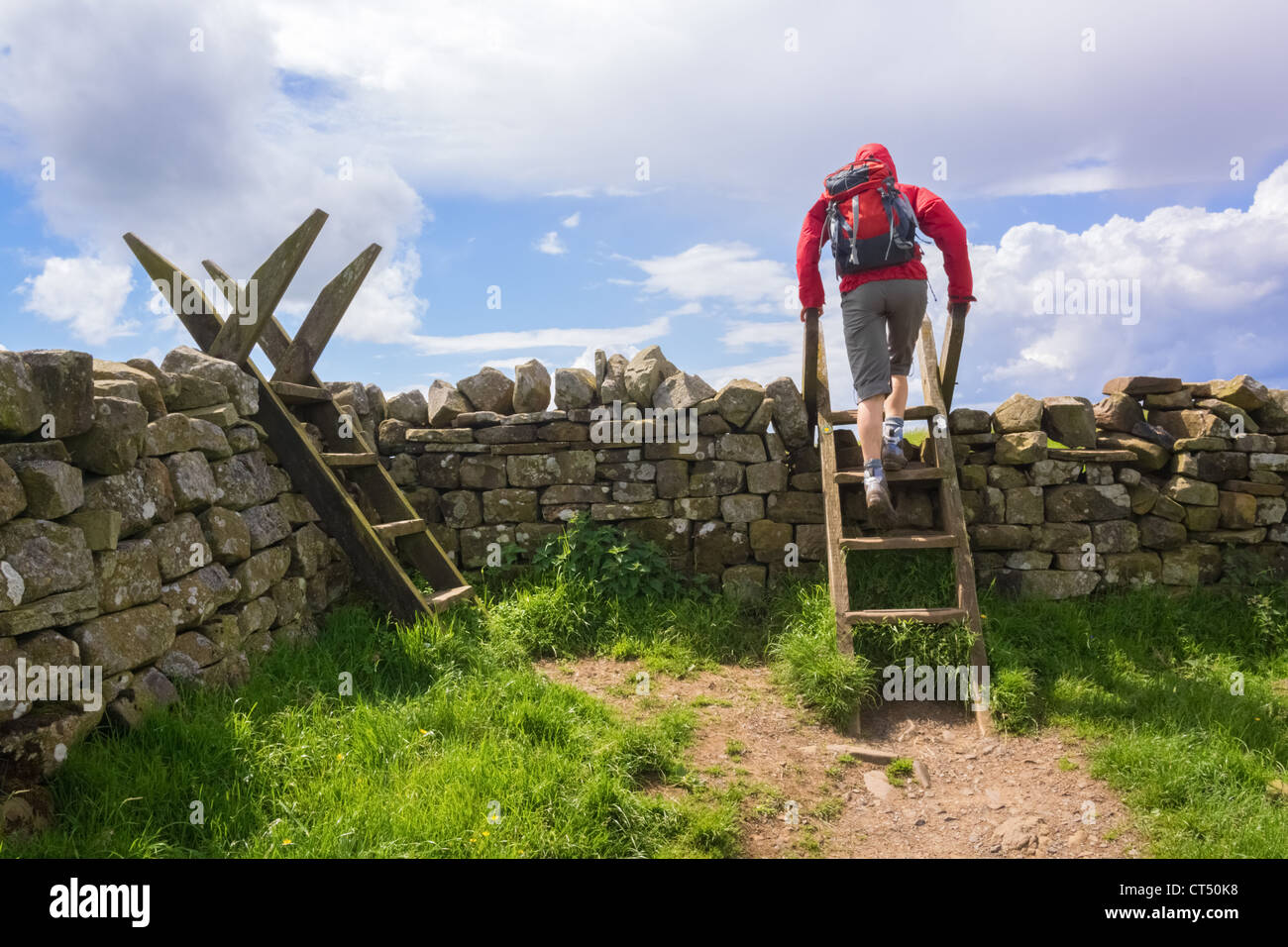 A hiker crosses a stile on the Hadrians Wall Walk at Crag Lough in Northumberland, England, UK. Stock Photo