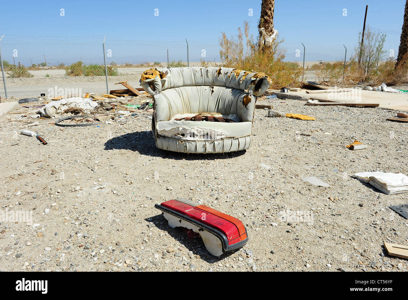 Abandoned upholstered chair, Salton Sea Beach, California USA Chair with car brake light in foreground, chain link fence behind. Stock Photo