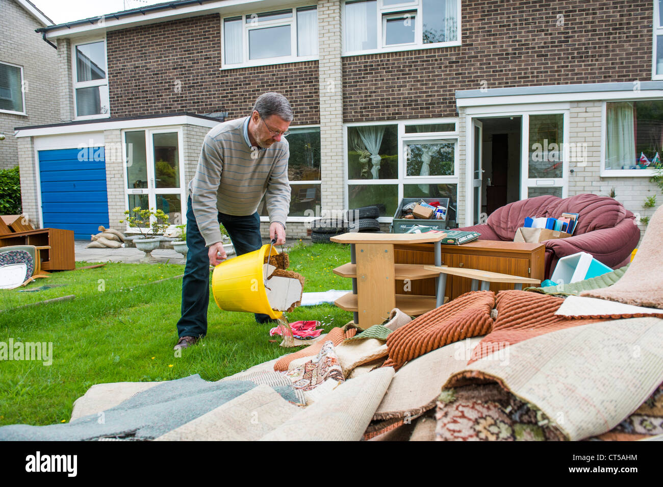 A man works clearing the damage done to his home Aberystwyth UK by floods June 2012 - dumping possessions on lawn outside house Stock Photo
