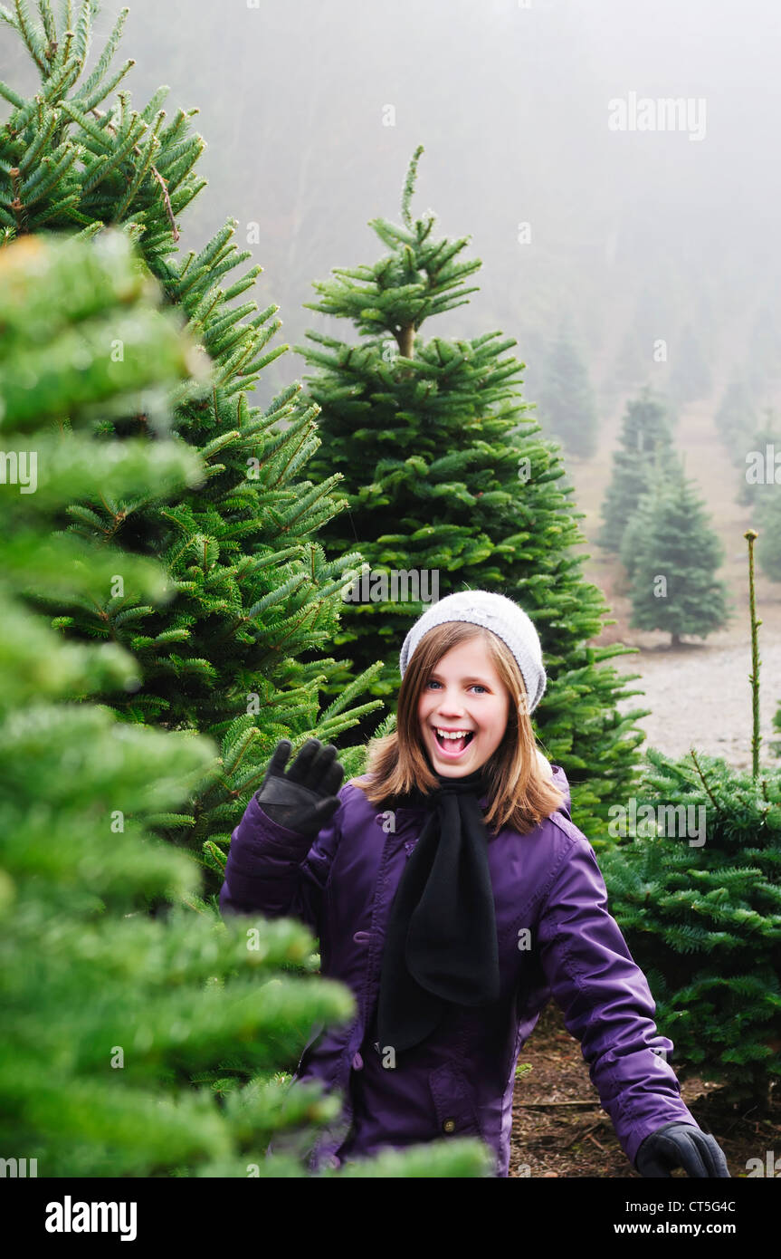A happy young girl waves from an evergreen tree nursery in the winter while she shops for a Christmas tree. Stock Photo