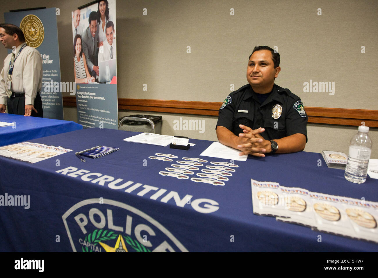 Hispanic male police officer sits at recruiting table during a job fair