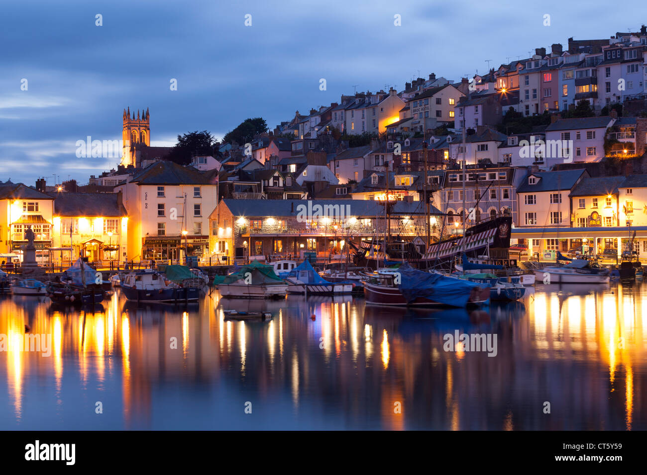 Brixham harbour at dusk, showing the Golden Hind and other small boats, with reflections of streetlights in the water. Stock Photo