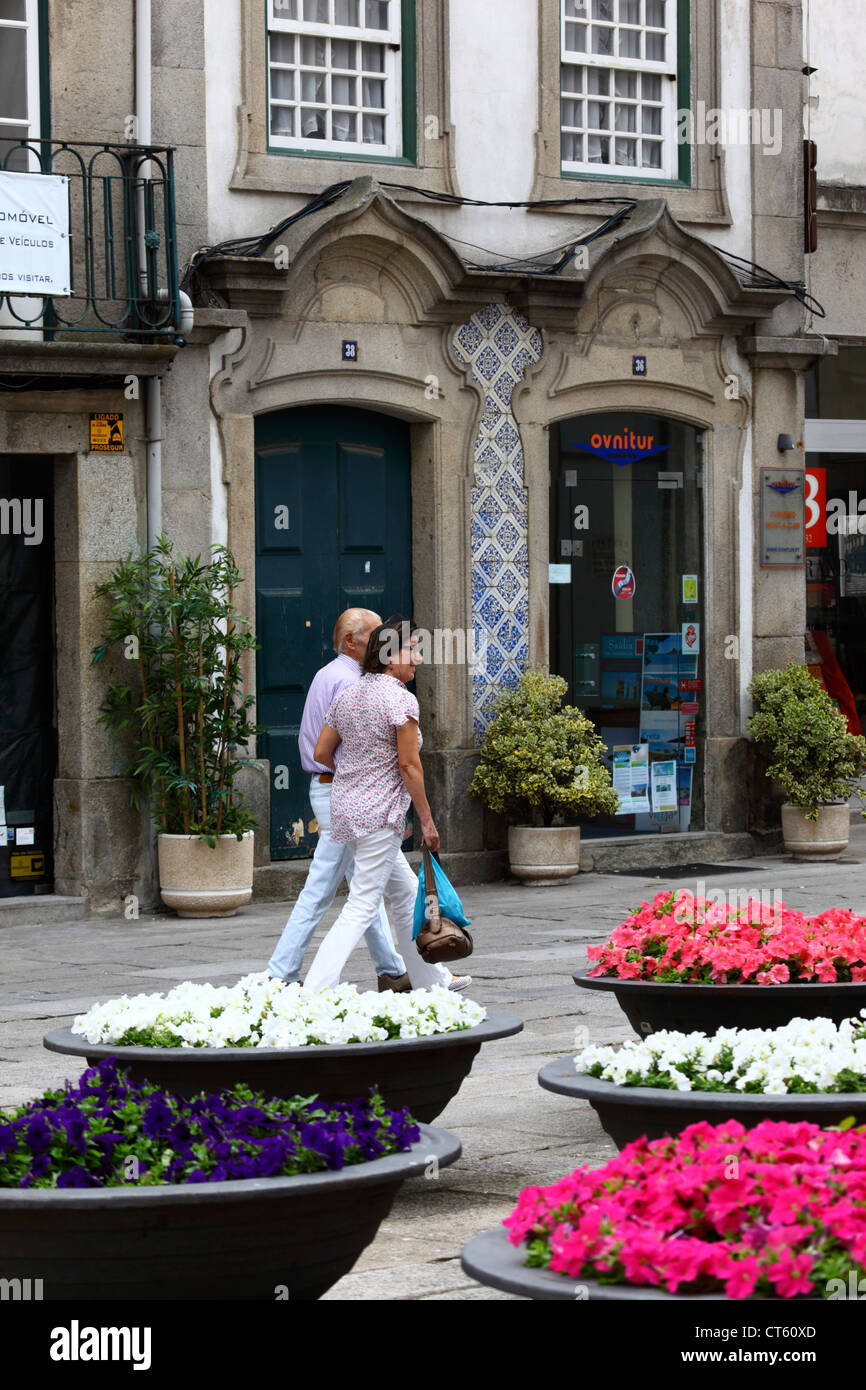 Couple walking past an ornate shop front and bowls of nasturtium flowers, Viana do Castelo, northern Portugal Stock Photo
