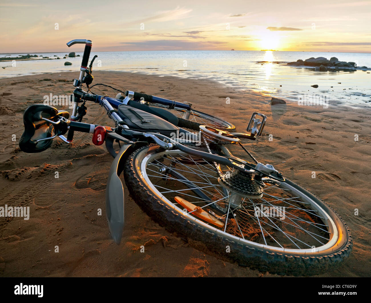 At the end of a journey. Bicycle lying on the beach in the light of setting Sun Stock Photo