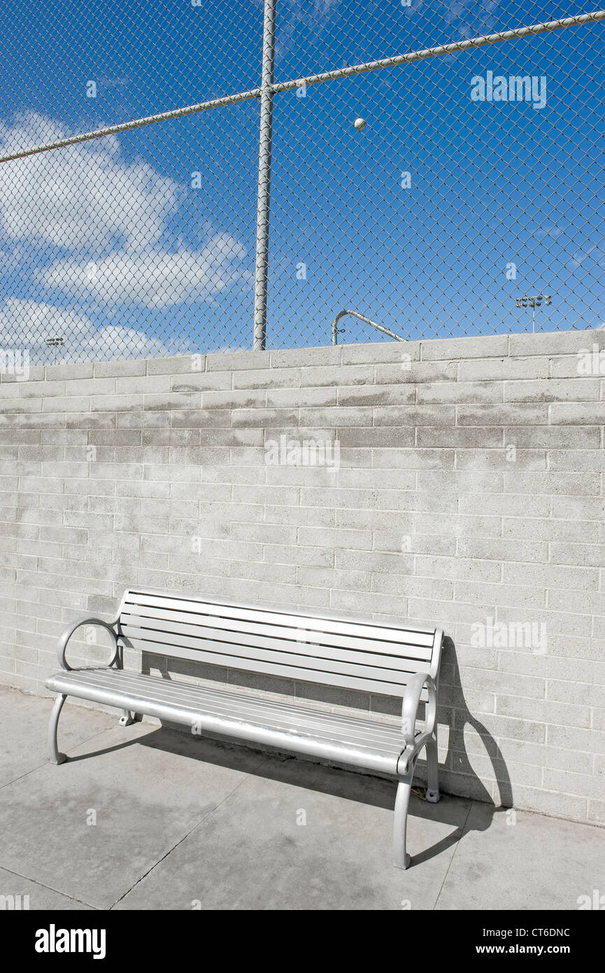 Metal bench on the side walk, above and behind is a ball stuck in a chain link fence. The location is Santa Monica, California. Stock Photo