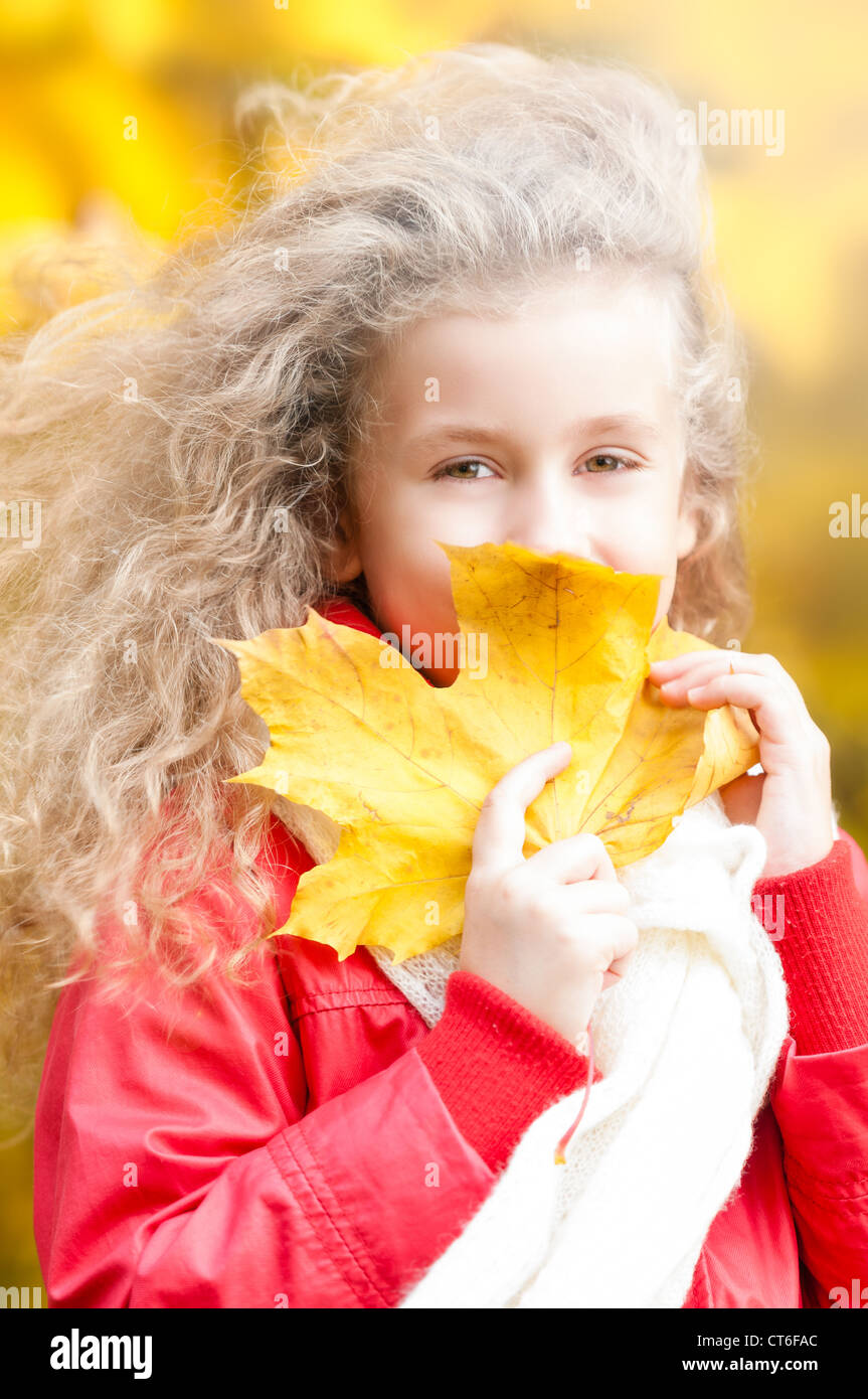 Beautiful and happy little girl holding yellow maple leaf at her face ...