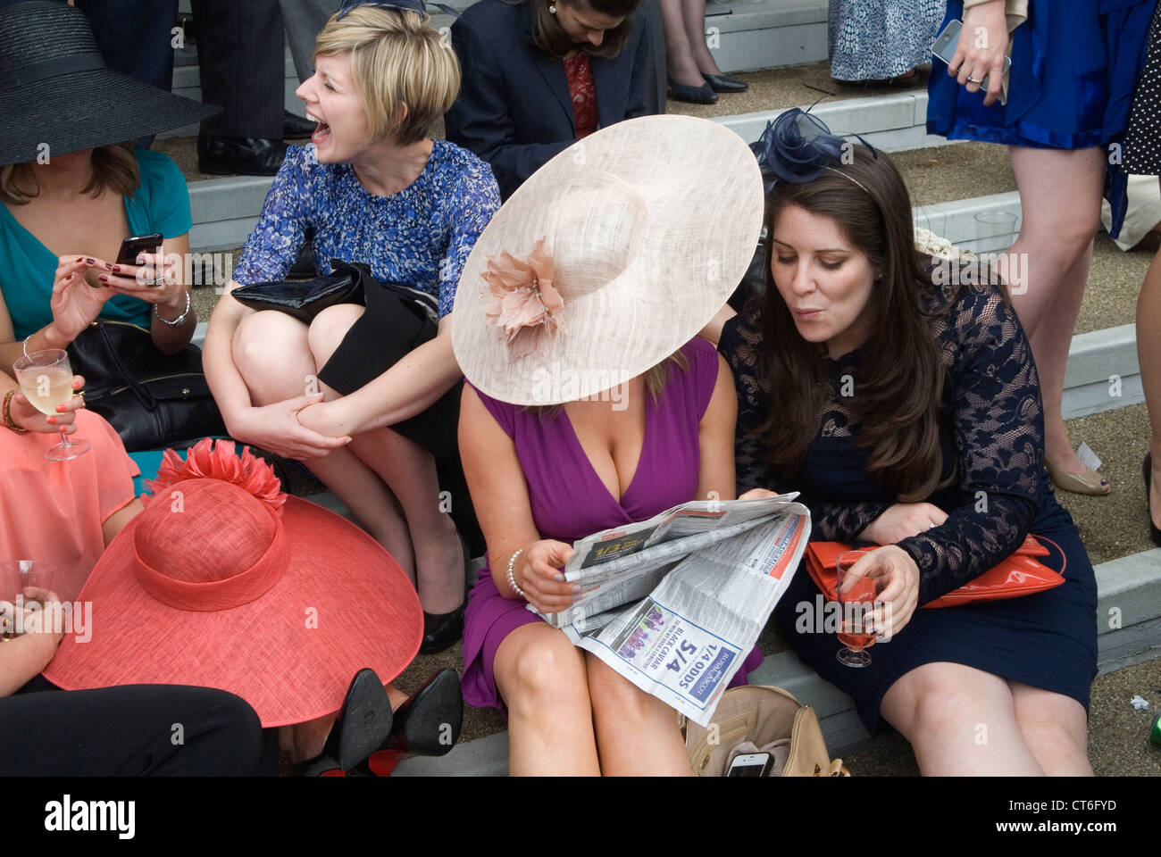New dress older woman showing her cleavage. Two women reading the newspaper together sitting down A day at the races, horse racing Royal Ascot, Berkshire England  2012, 2010s UK HOMER SYKES Stock Photo