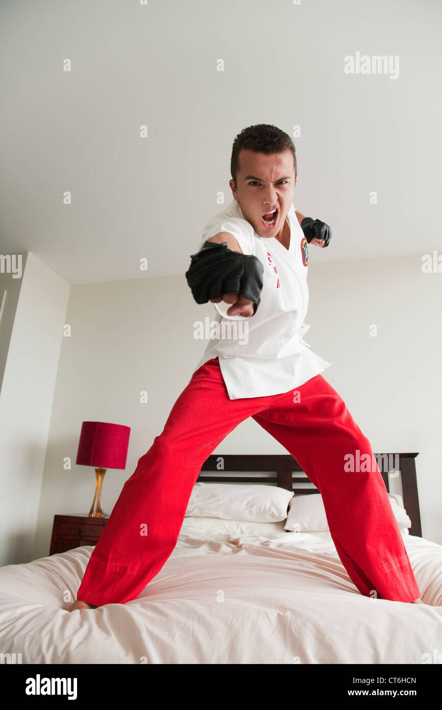 Portrait of an aggressive young man practicing kung fu on bed Stock