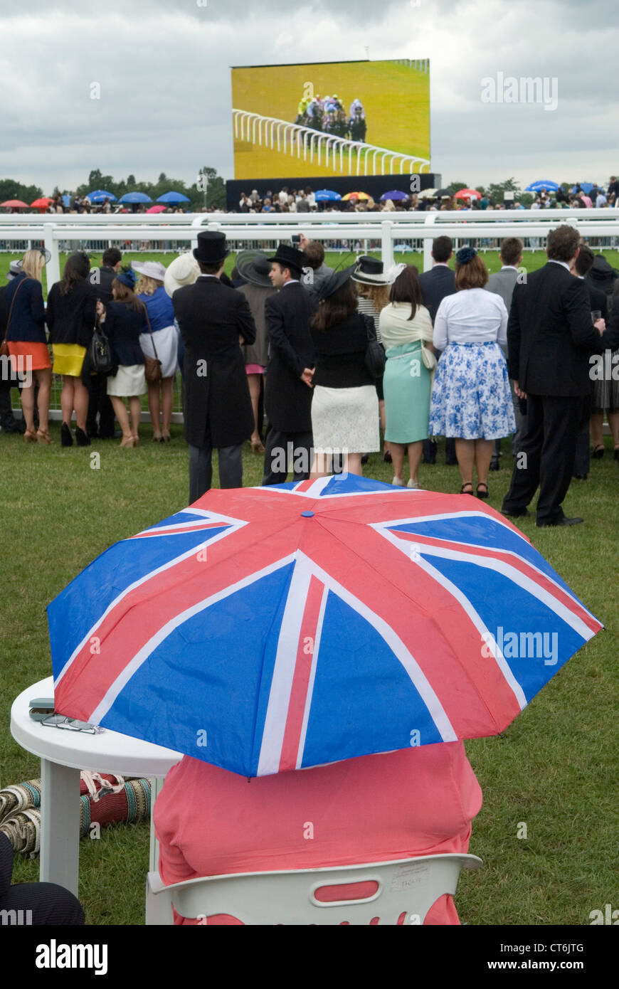 Union Jack umbrella rainy day Royal Ascot horse racing watching the horse runner on a huge outside broadcast television TV screen Berkshire 2012 2010s UK HOMER SYKES Stock Photo