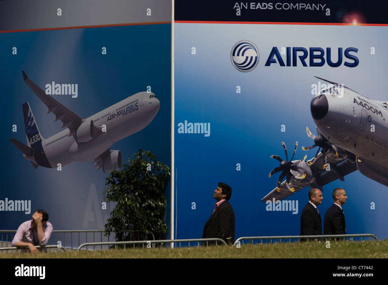 Delegates walk past a billboard of A380 airliner and military A400M transporter outside an EADS chalet at the Farnborough Air Show Stock Photo