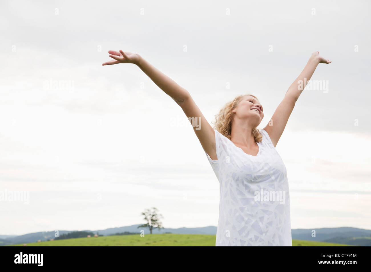 young woman on meadow raising her arms in the air Stock Photo