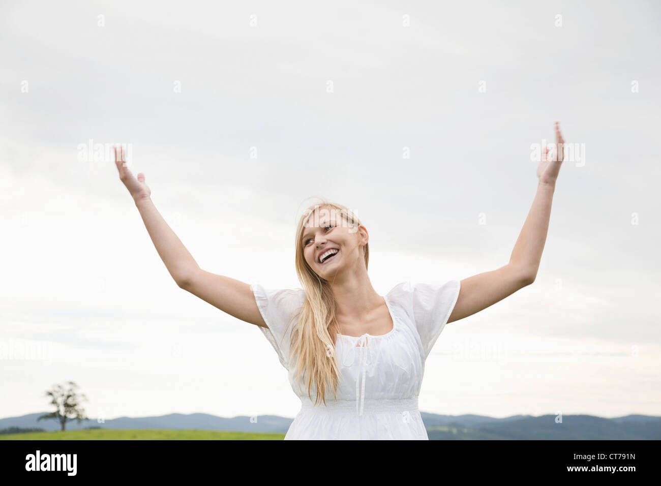 young woman on meadow raising her arms in the air Stock Photo