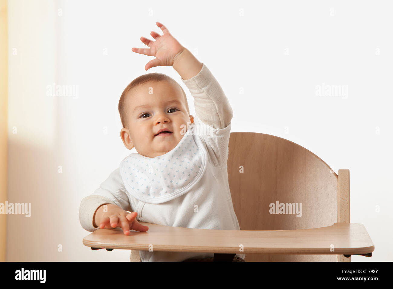 portrait of baby sitting in high chair waving Stock Photo Alamy