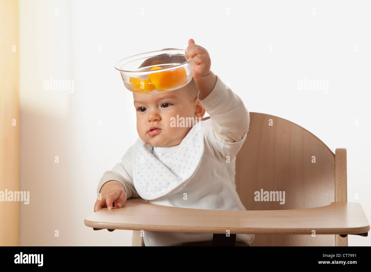 portrait of baby in high chair holding bowl with fruit Stock Photo