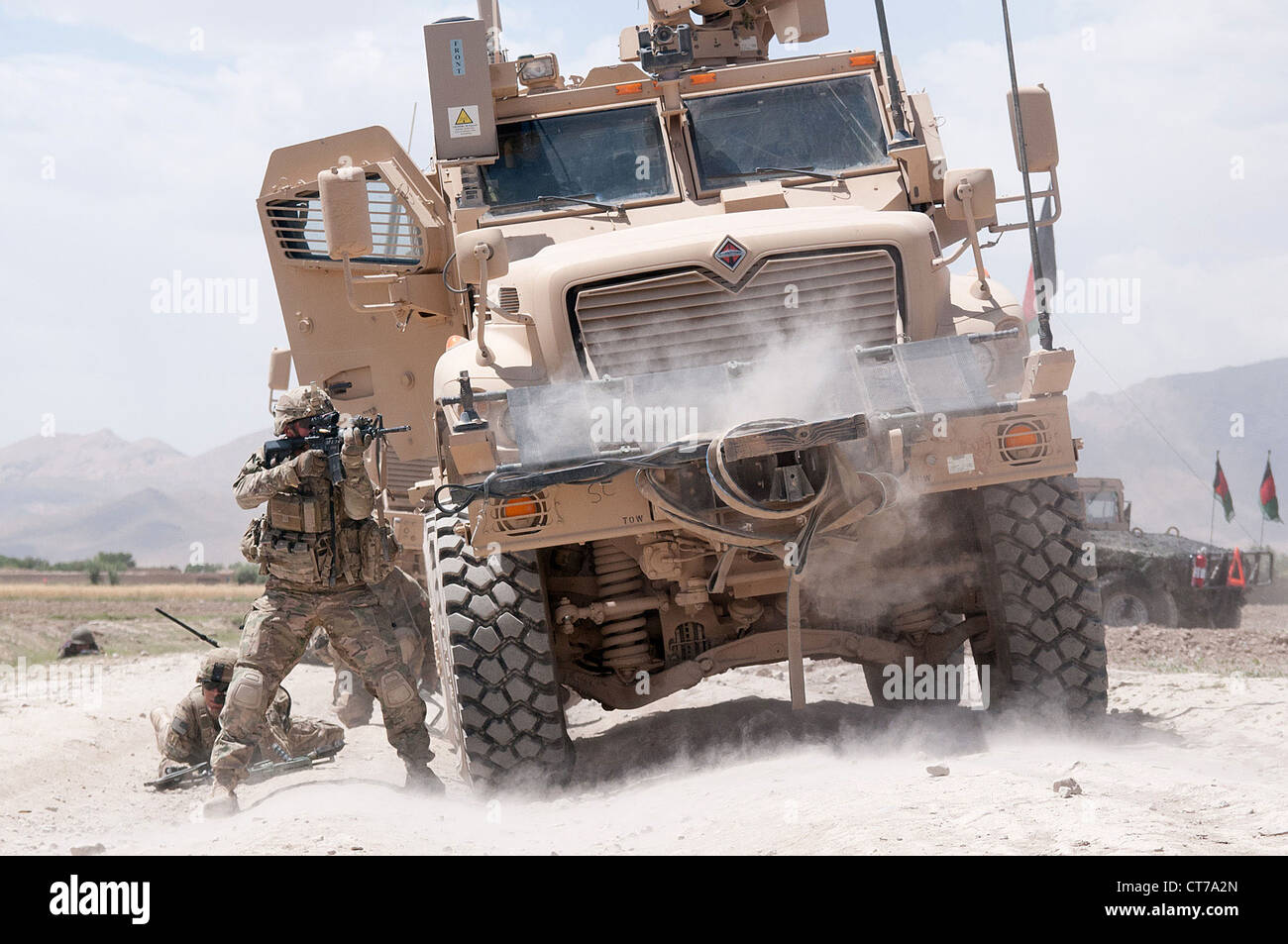 A US Army paratrooper with the 82nd Airborne Division fires his M4 carbine at insurgents during a firefight June 30, 2012 in Ghazni Province, Afghanistan. The vehicle he is using for cover is a Mine Resistant Ambush Protected vehicle. Stock Photo