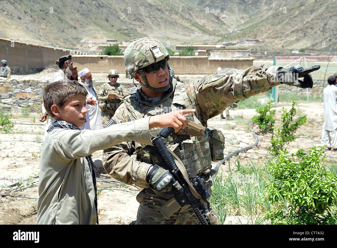 A US Army soldier speaks to a local teenager about the location of his school during a visit to the Central Kunar Demo Farm June 21, 2012 in Kunar, Afghanistan. The soldier is part of the Provincial Reconstruction Team Kunar agricultural section who assiss the demo farm to show the farmers and other locals nearby more effective ways to cultivate crops. Stock Photo