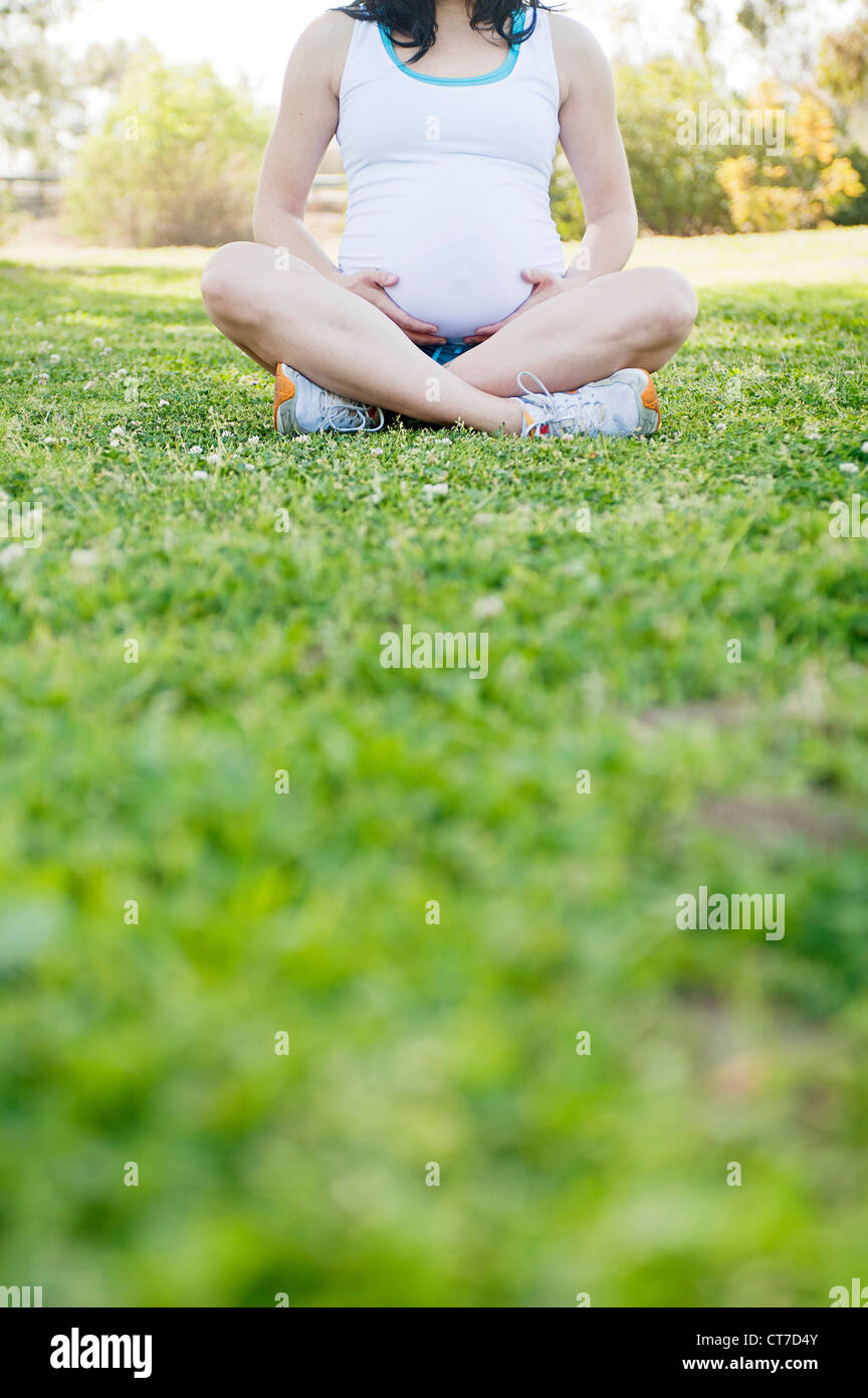 Pregnant young woman sitting cross legged on grass Stock Photo Alamy