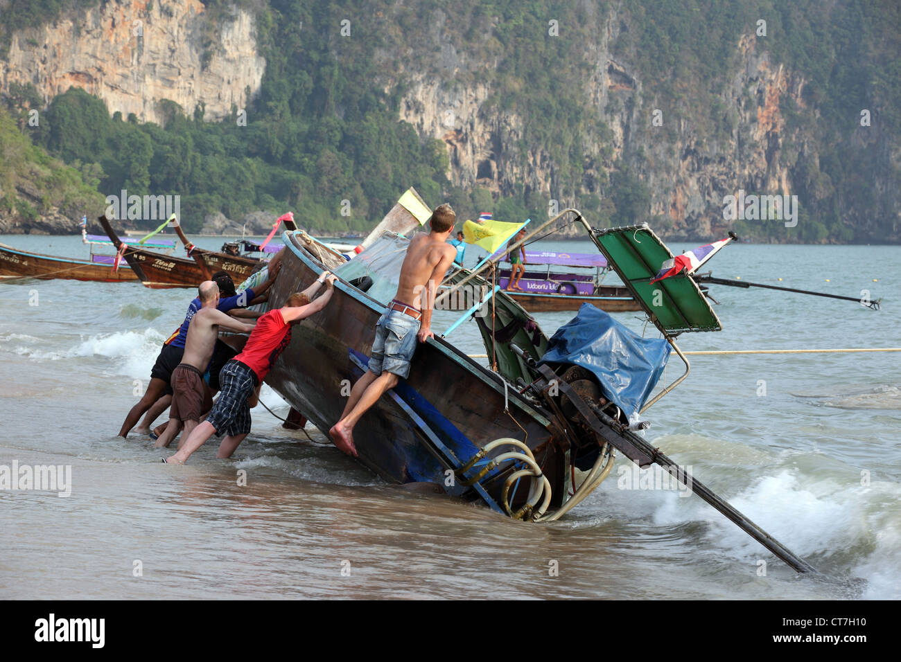 Tourists help to upright a long tail wooden boat on Ao Nang Beach in Krabi, Thailand Stock Photo