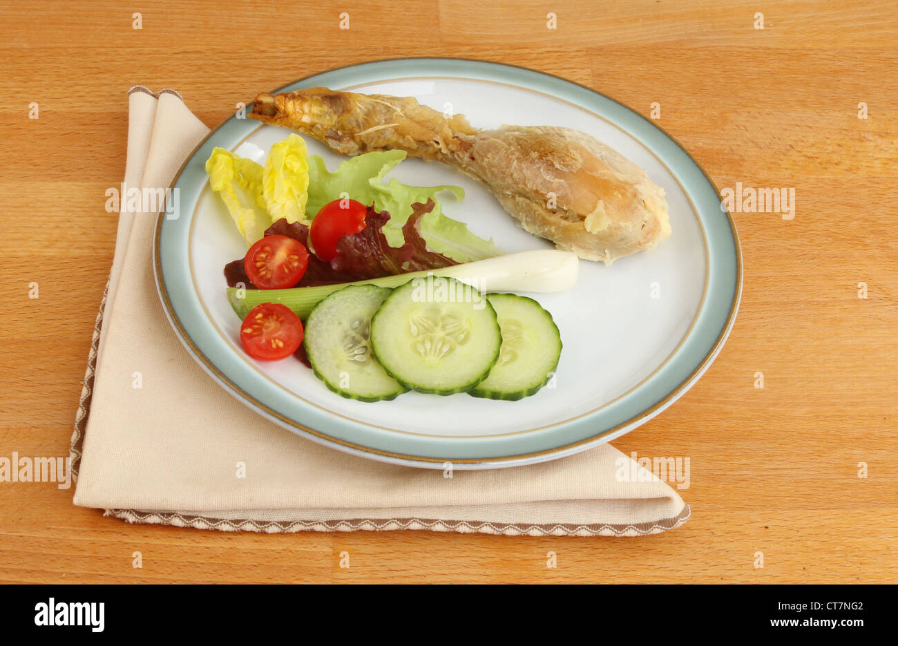 Chicken drumstick salad on a plate with a serviette on a wooden surface Stock Photo